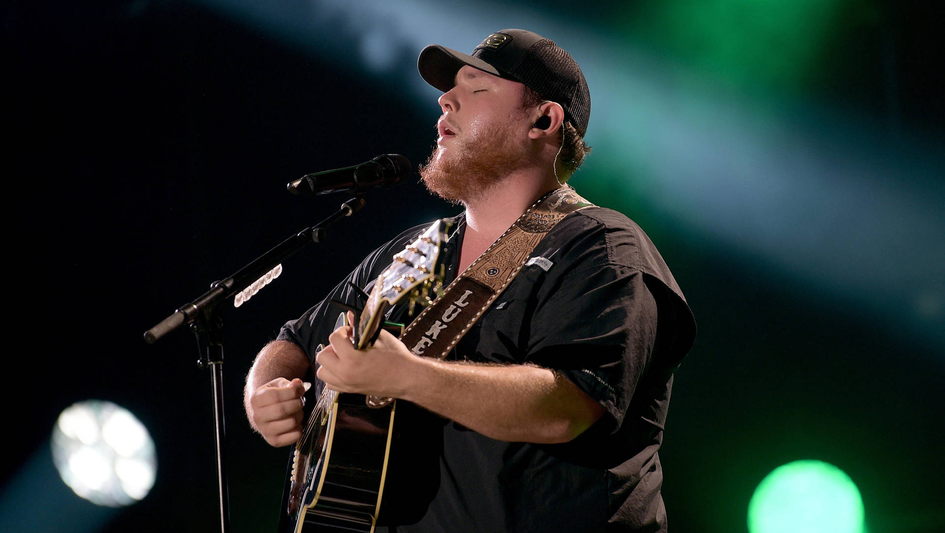 A Man In A Black Hat Singing Into A Microphone Background