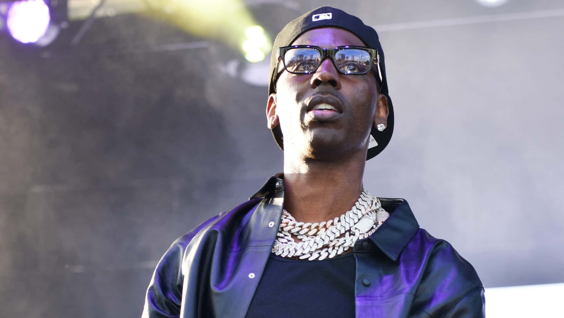 A Man In A Black Jacket And Sunglasses Is Standing On Stage Background