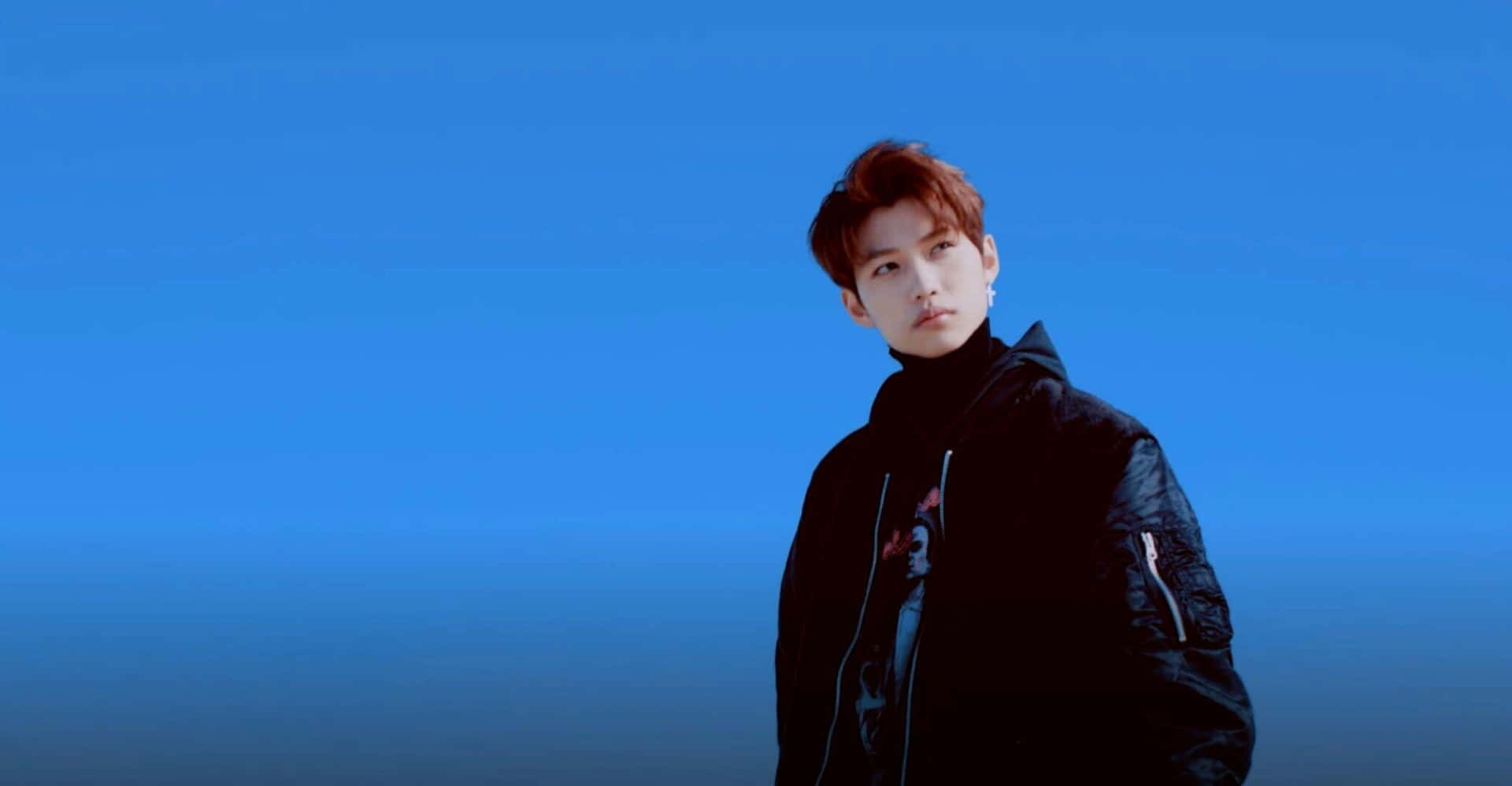 A Man In A Black Jacket Standing In Front Of A Blue Sky Background