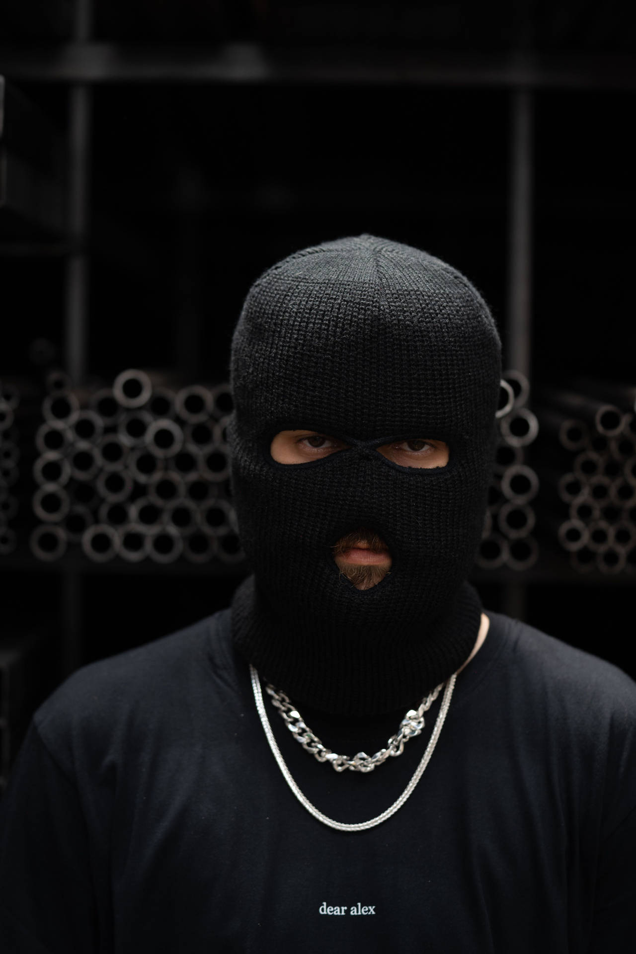 A Man In A Black Mask Standing In Front Of A Rack Background