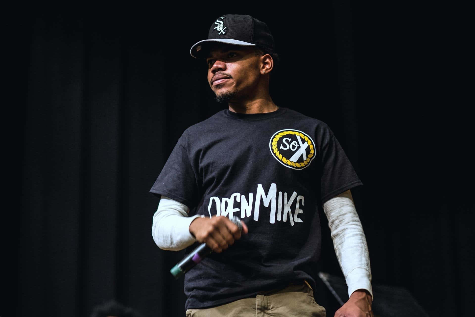 A Man In A Black Shirt Standing On Stage Background