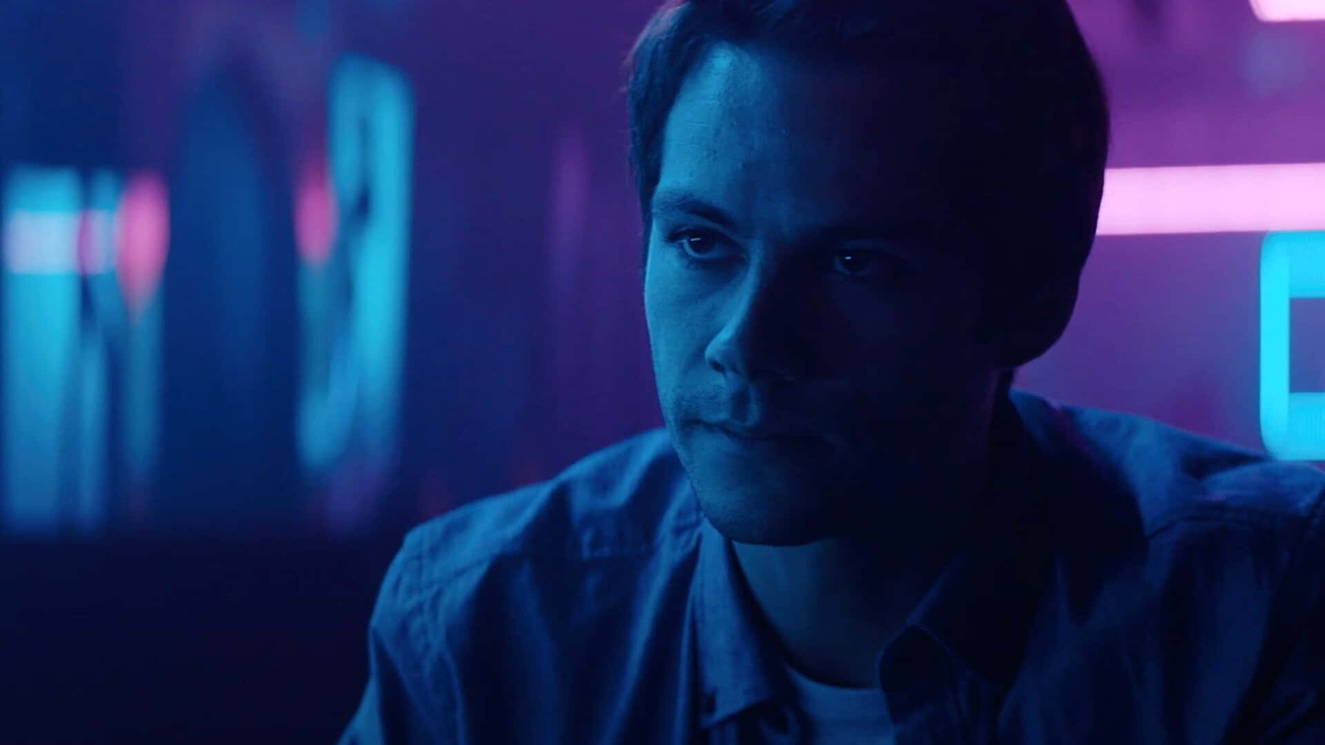 A Man In A Blue Shirt Is Staring At A Neon Light Background