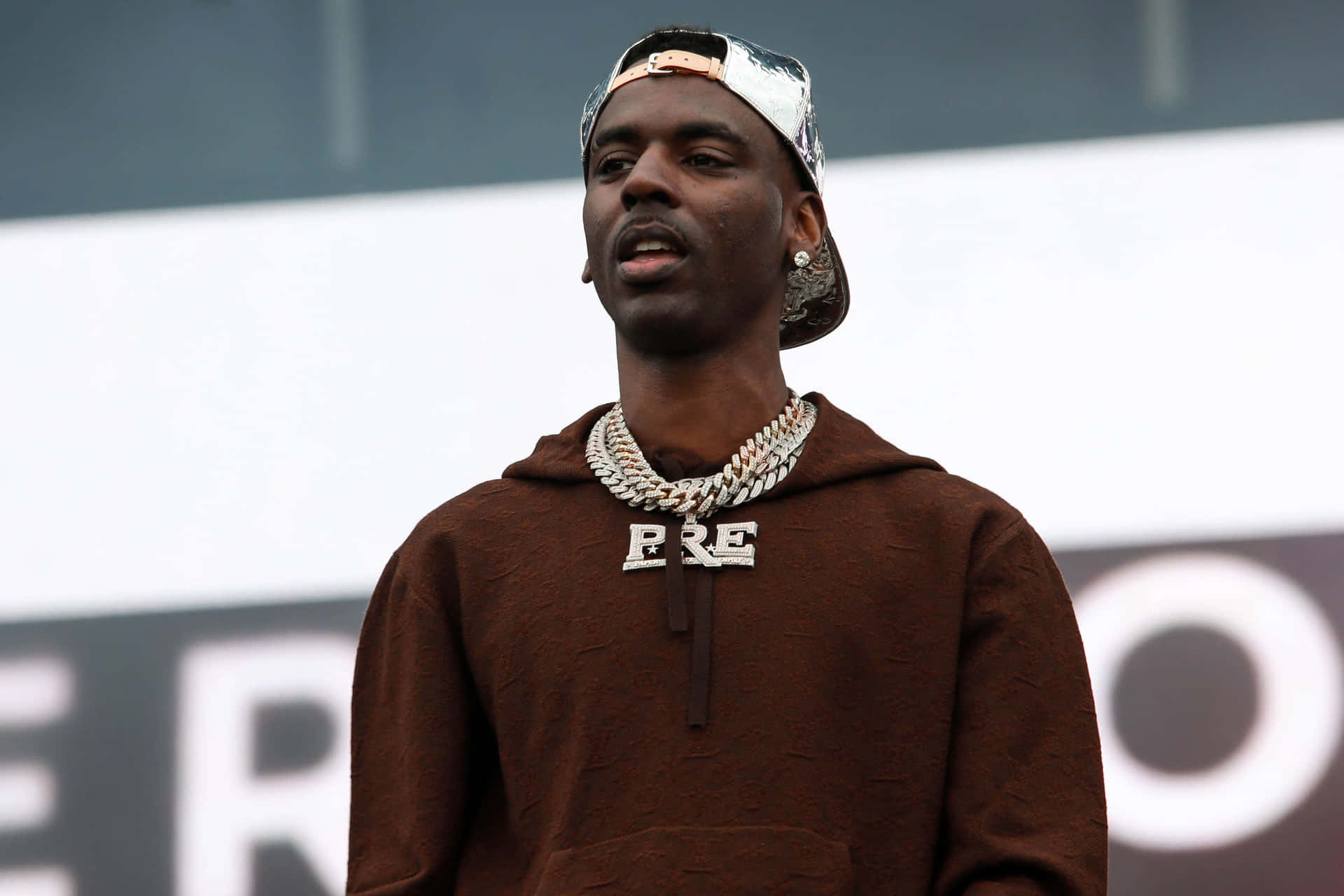 A Man In A Brown Hoodie Is Standing On Stage Background