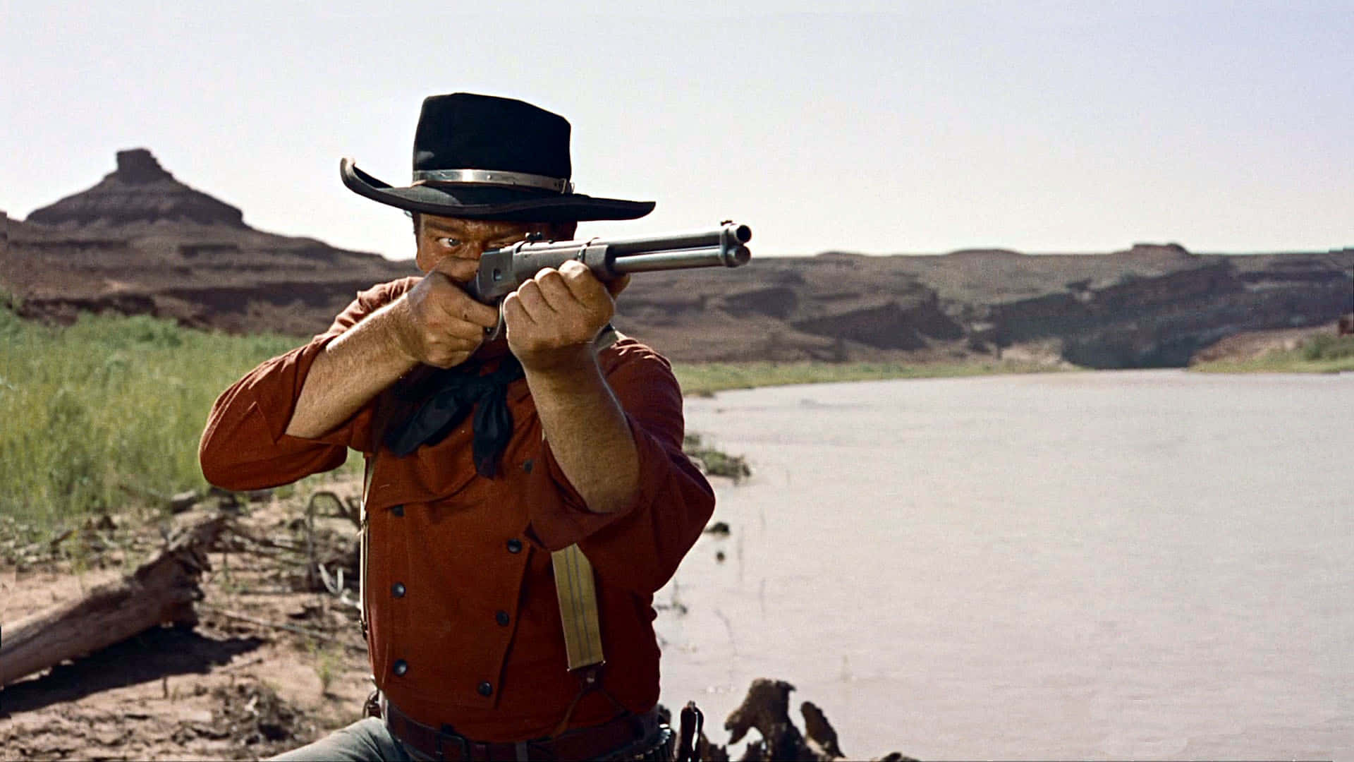 A Man In A Cowboy Hat Is Holding A Gun Background
