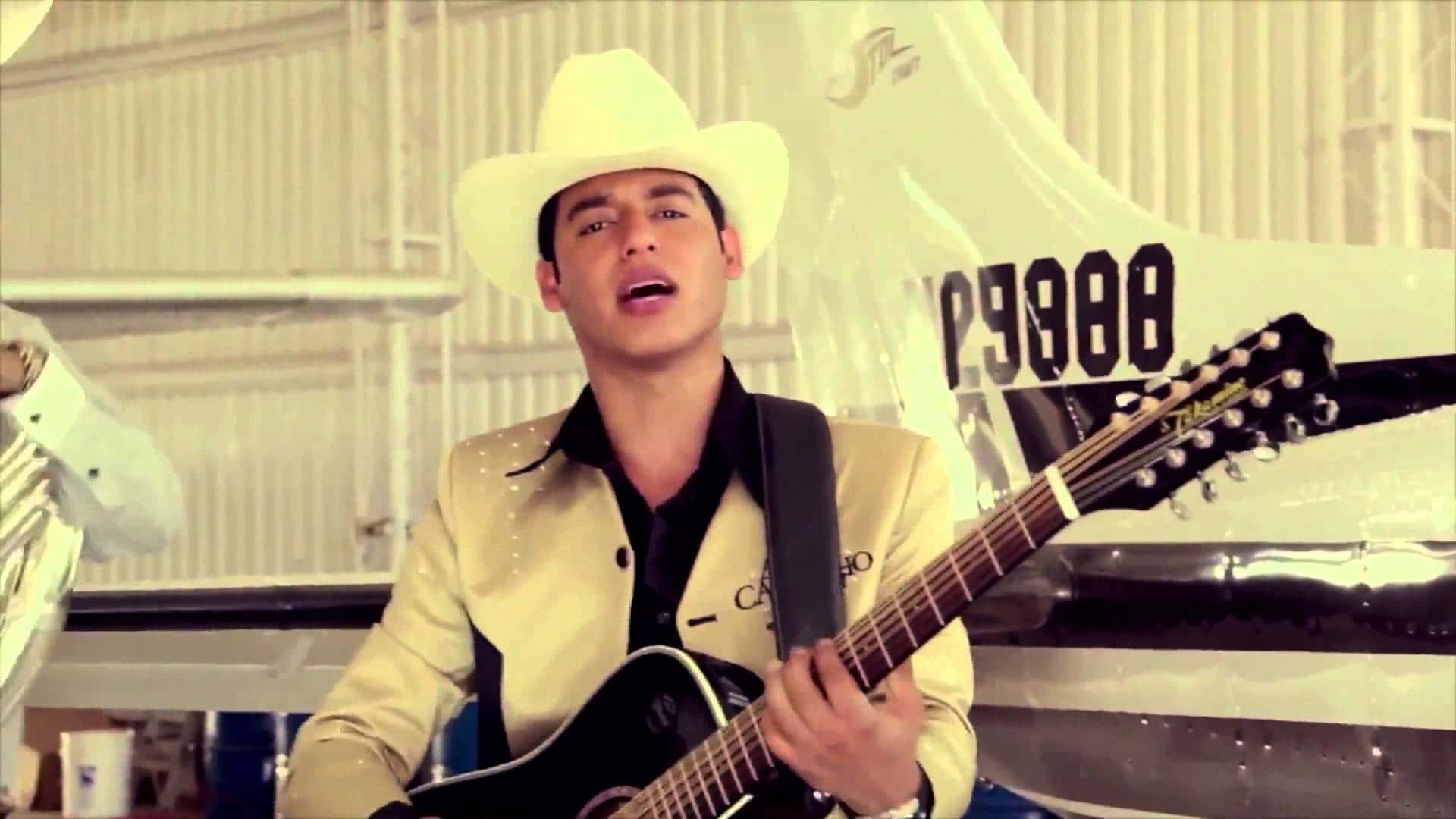 A Man In A Cowboy Hat Is Playing Guitar In Front Of A Plane Background