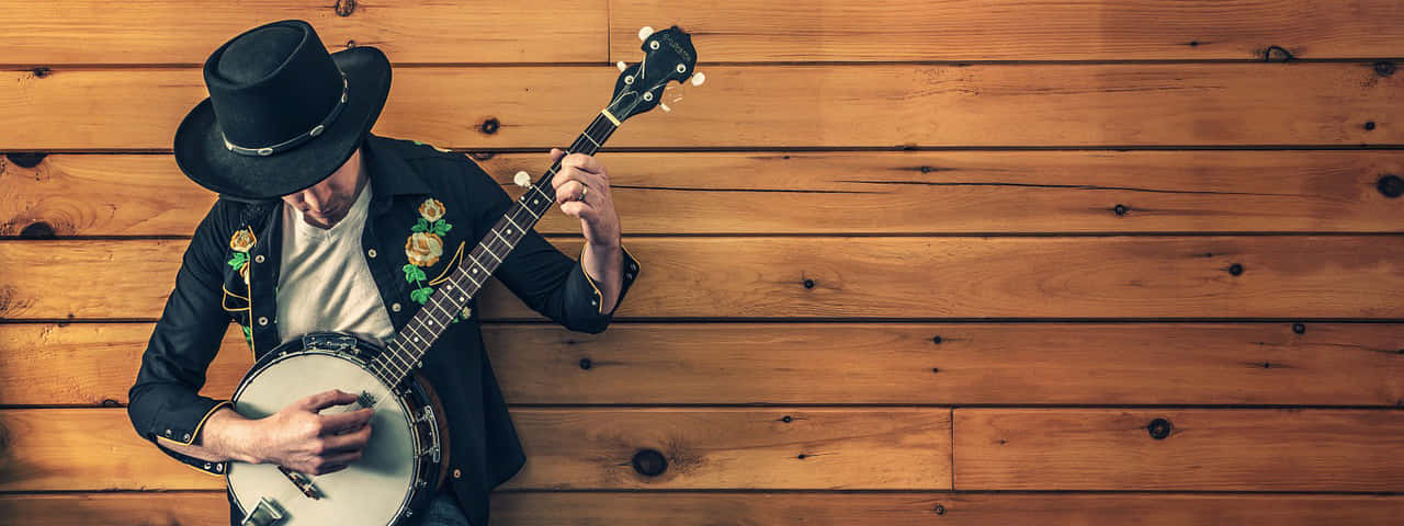 A Man In A Cowboy Hat Playing A Banjo Background