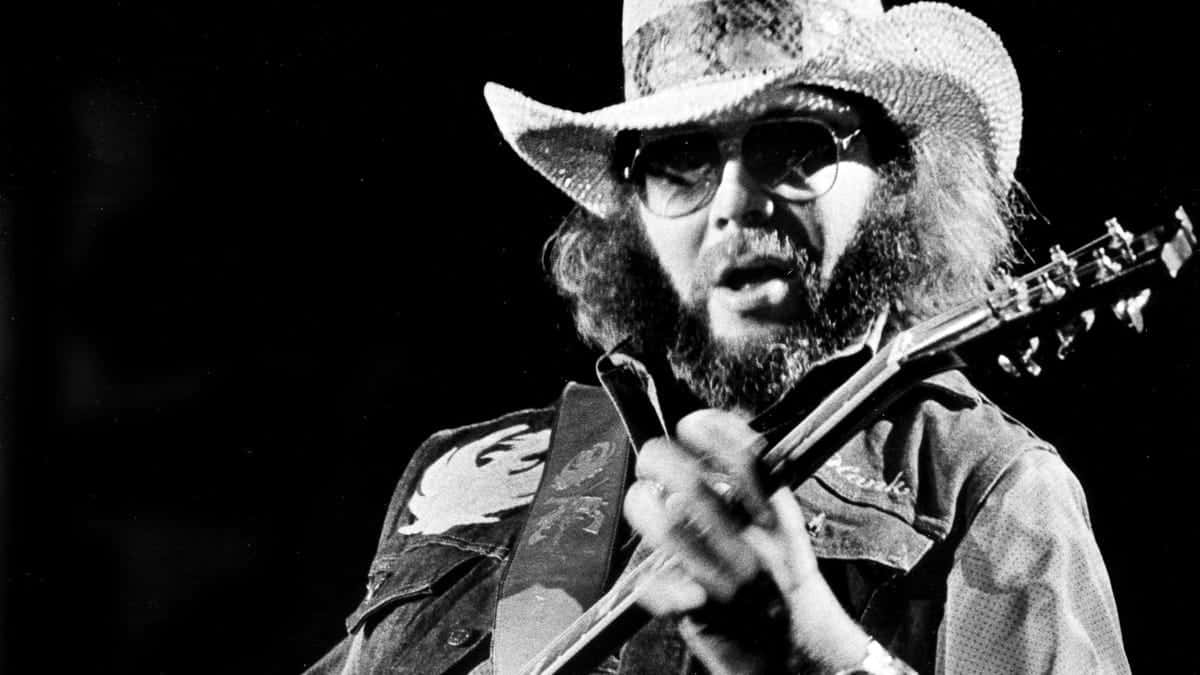 A Man In A Cowboy Hat Playing A Guitar Background