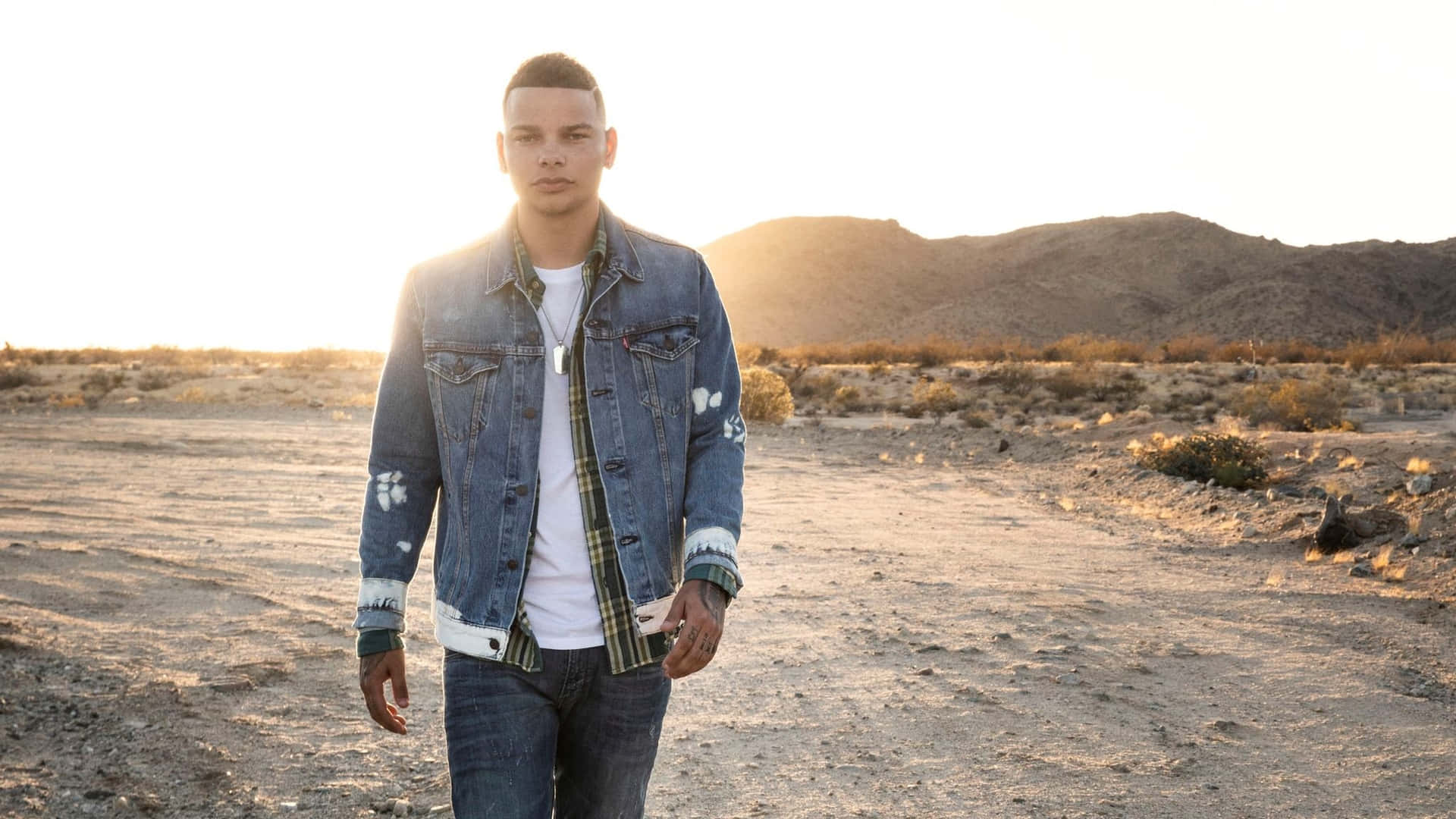 A Man In A Denim Jacket Standing In The Desert Background