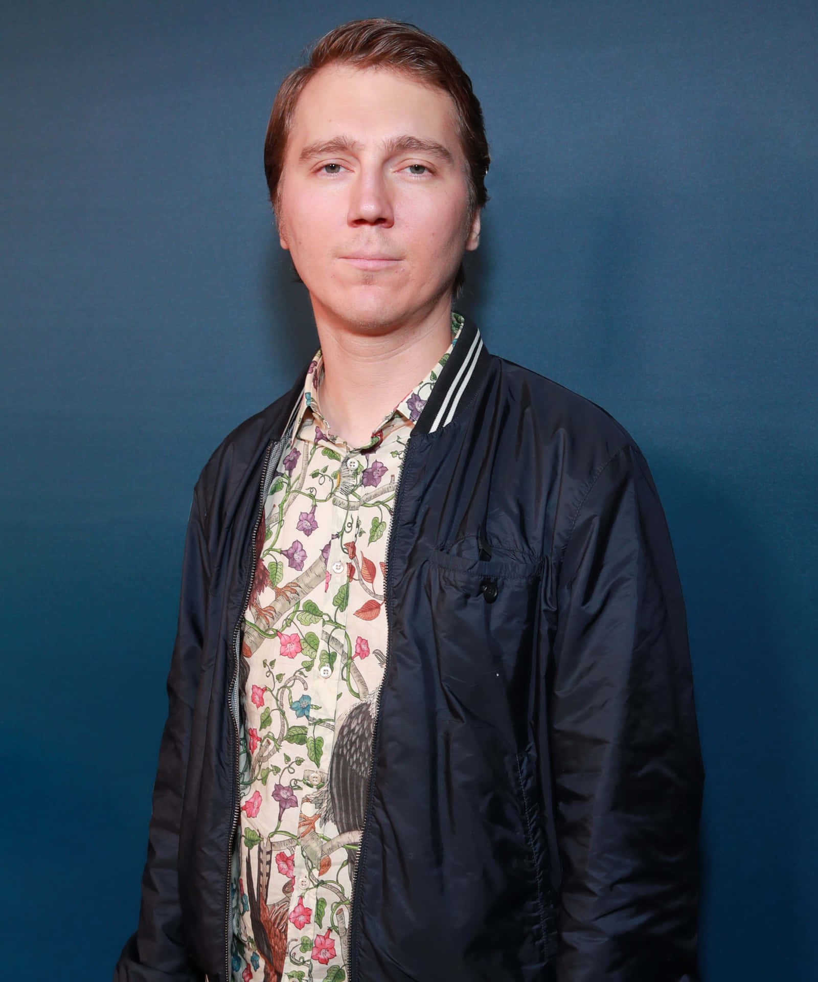 A Man In A Floral Shirt Standing In Front Of A Blue Wall Background