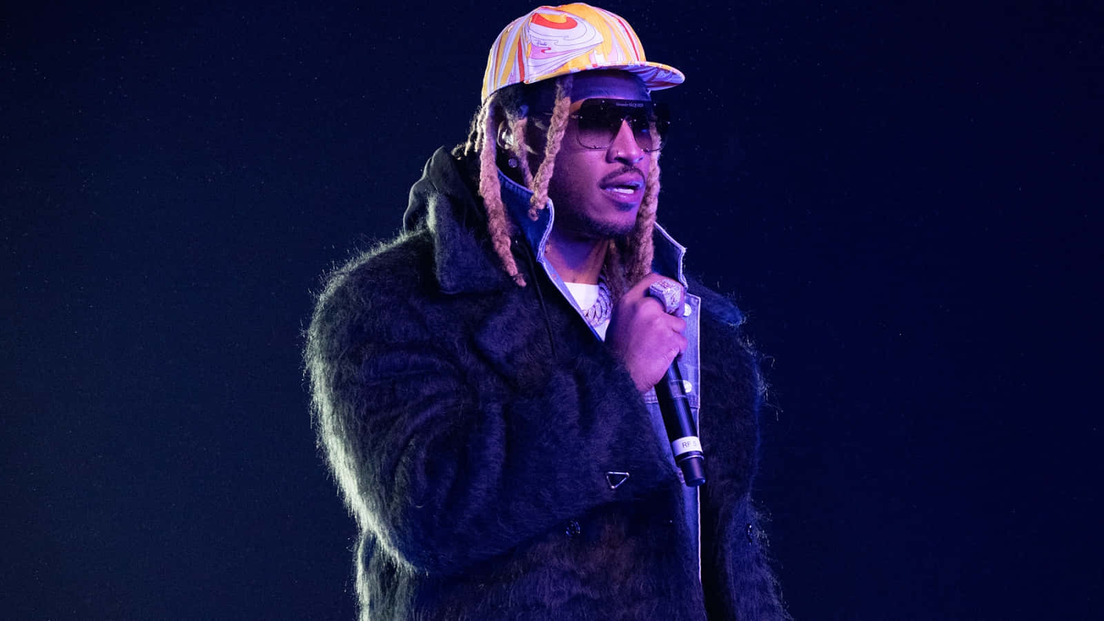 A Man In A Fur Coat And Hat Is Holding A Microphone Background