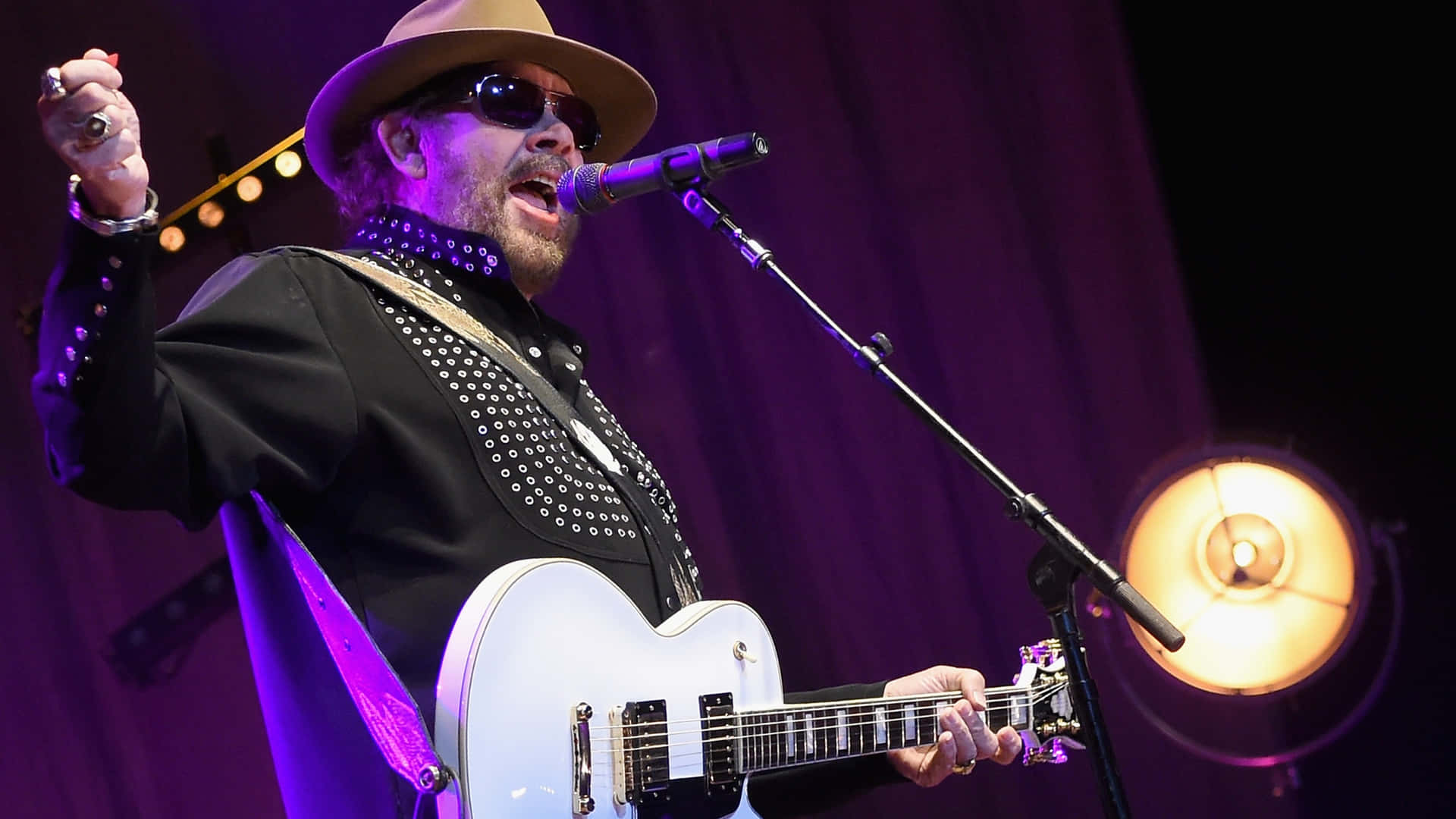 A Man In A Hat And Hat Playing A Guitar Background