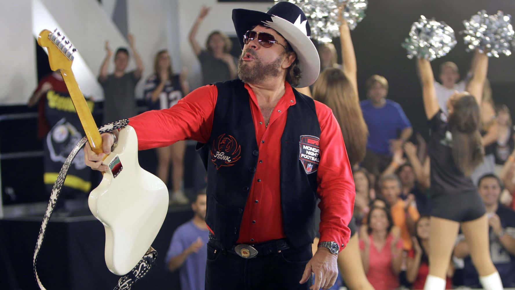 A Man In A Hat And Red Vest Holding A Guitar Background