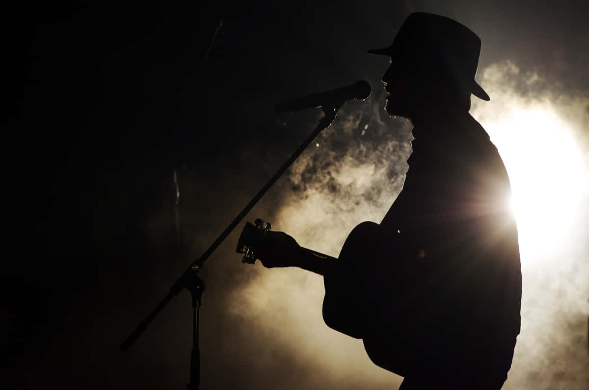 A Man In A Hat Is Playing An Acoustic Guitar Background