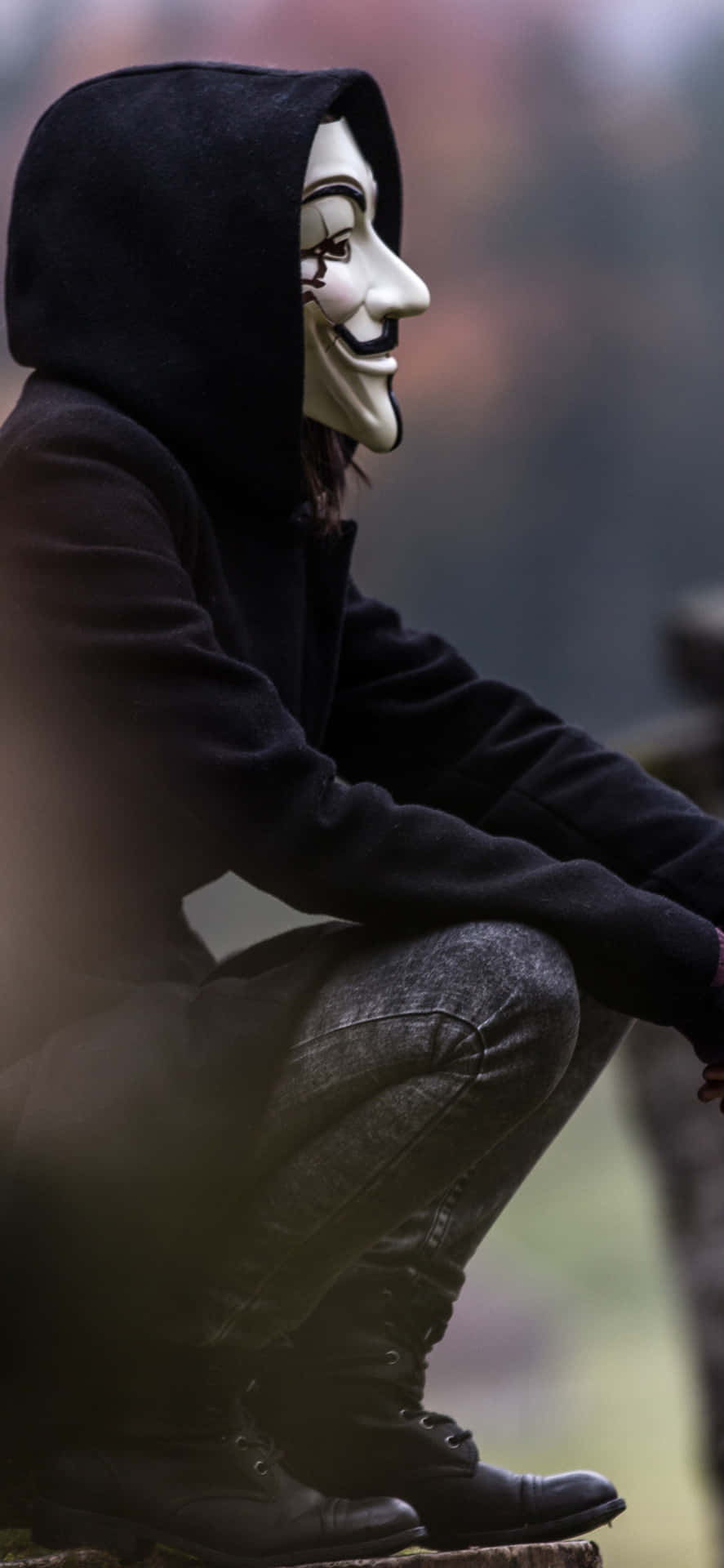 A Man In A Hoodie And Mask Sitting On A Rock