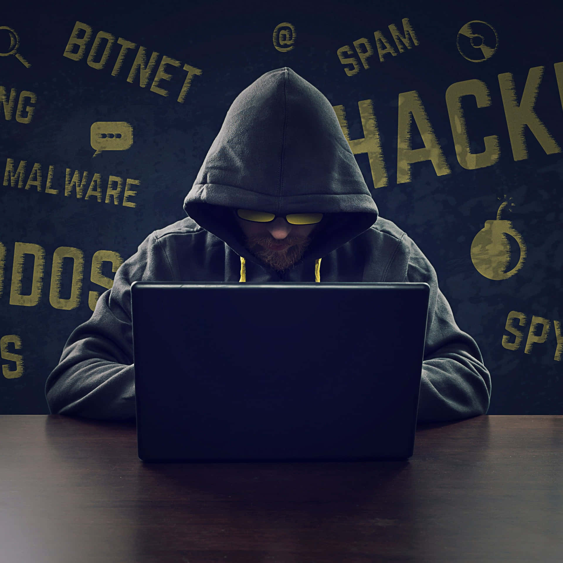 A Man In A Hoodie Is Sitting At A Table With A Laptop Background