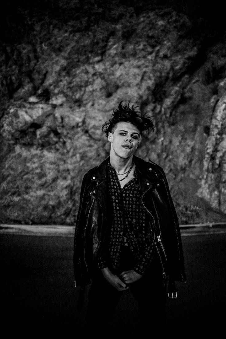 A Man In A Leather Jacket Standing In Front Of A Rock Background