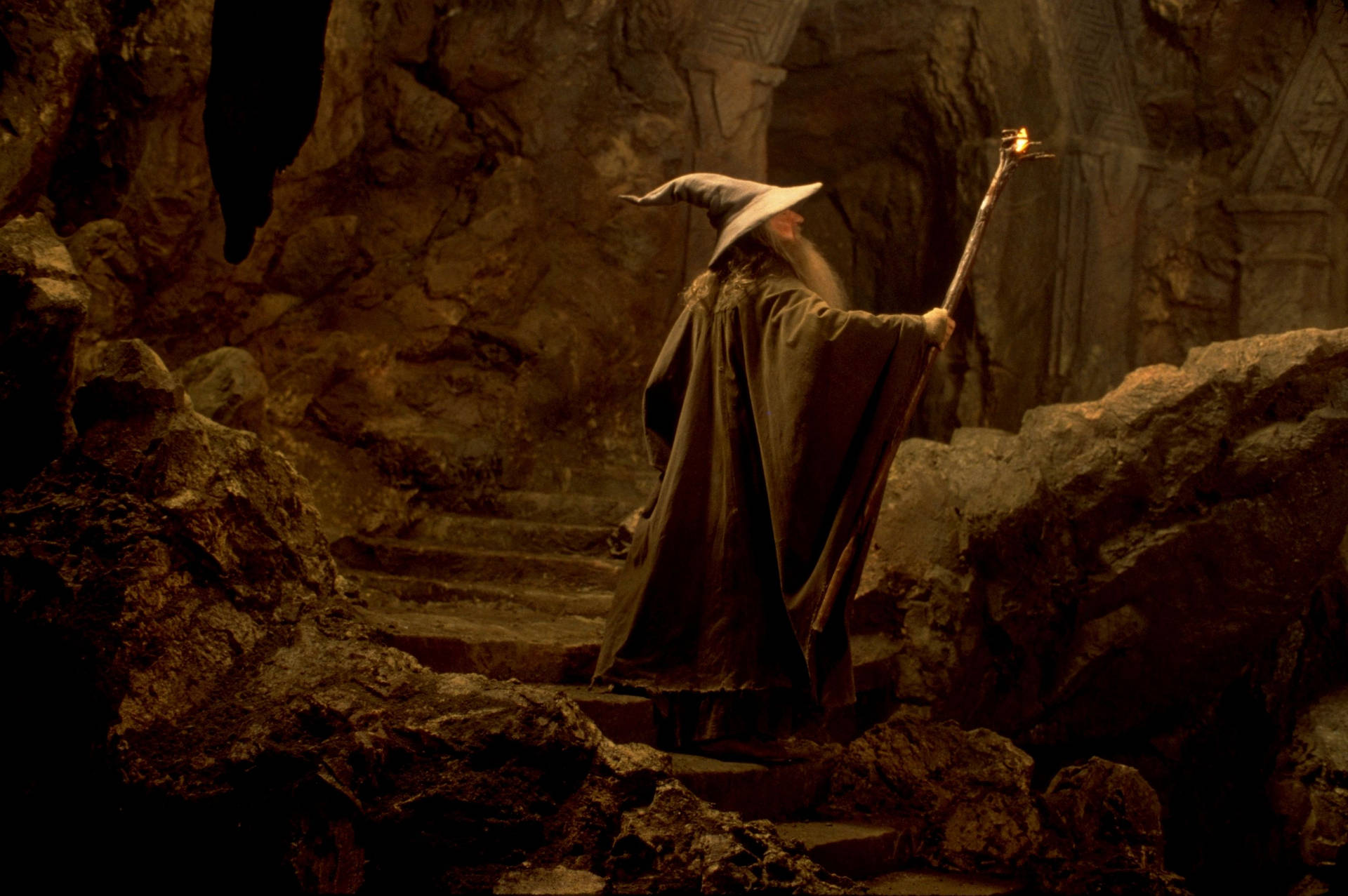 A Man In A Robe Is Standing In A Cave Background