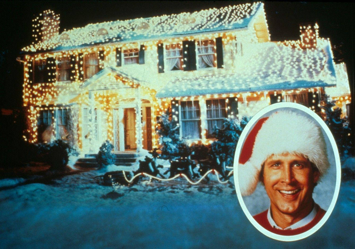 A Man In A Santa Hat Is Standing In Front Of A House With Lights Background