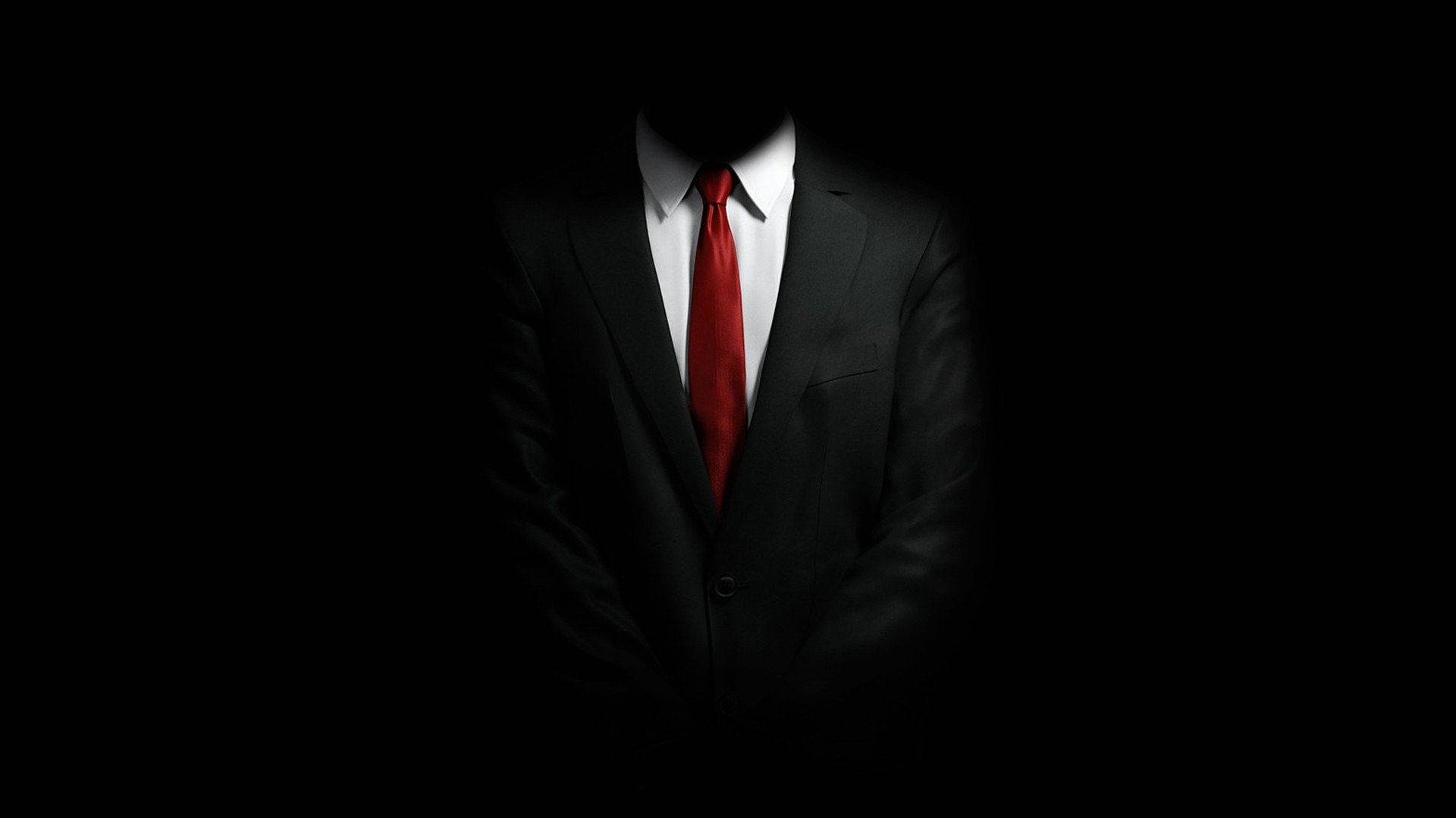 A Man In A Suit And Tie Is Standing In The Dark Background