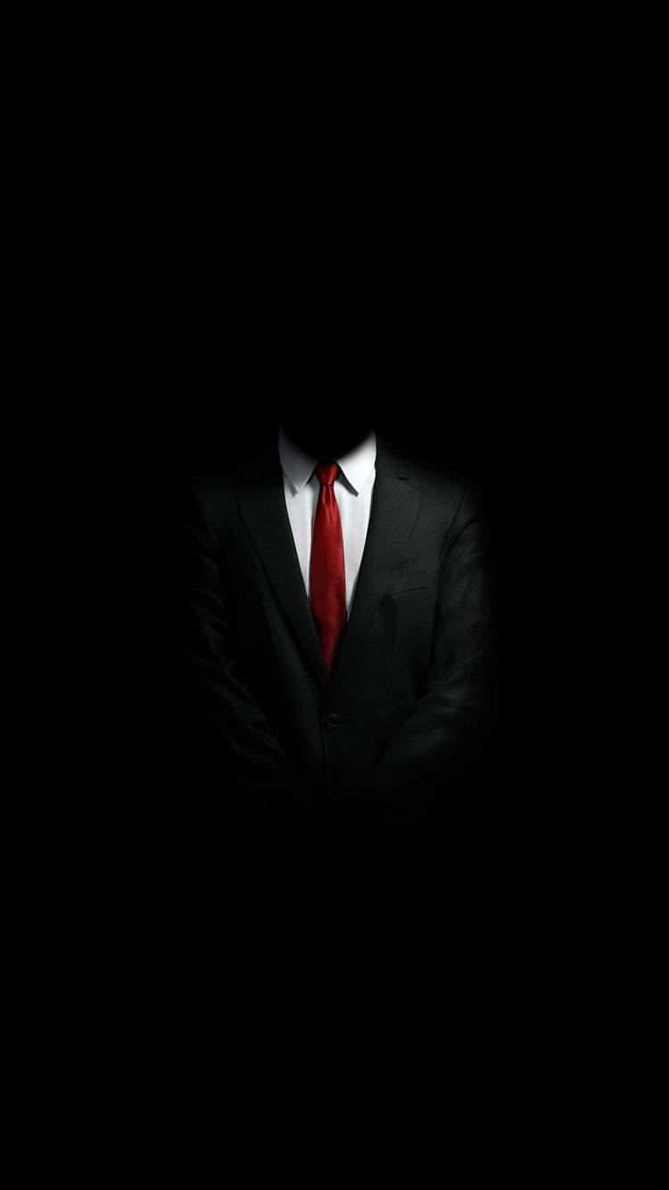 A Man In A Suit And Tie Is Standing In The Dark Background