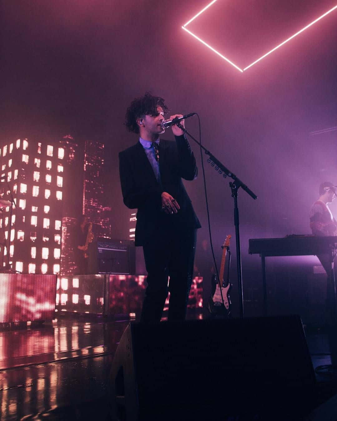 A Man In A Suit Singing On Stage Background
