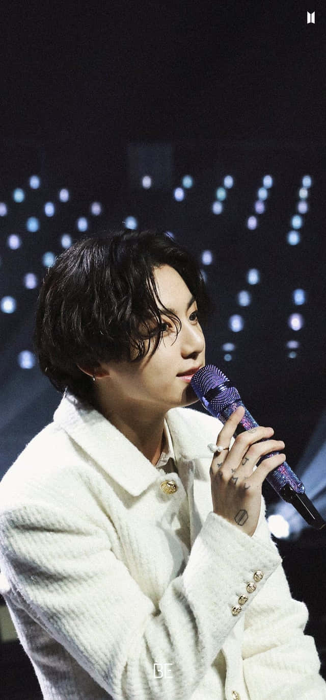 A Man In A White Jacket Is Holding A Microphone Background