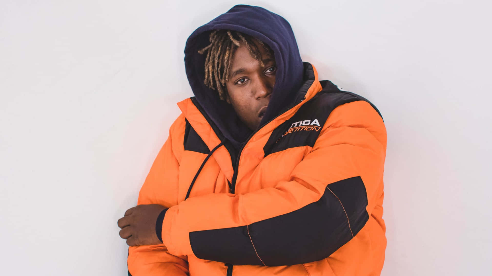 A Man In An Orange Jacket Leaning Against A Wall Background