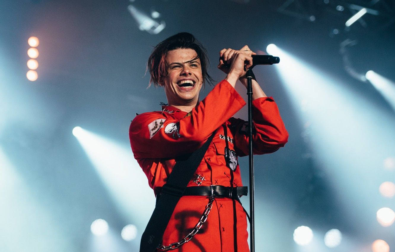 A Man In Red Is Singing Into A Microphone Background