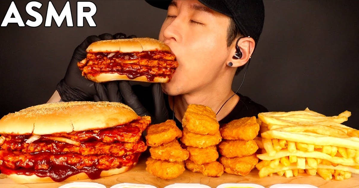 A Man Is Eating A Huge Burger With Fries