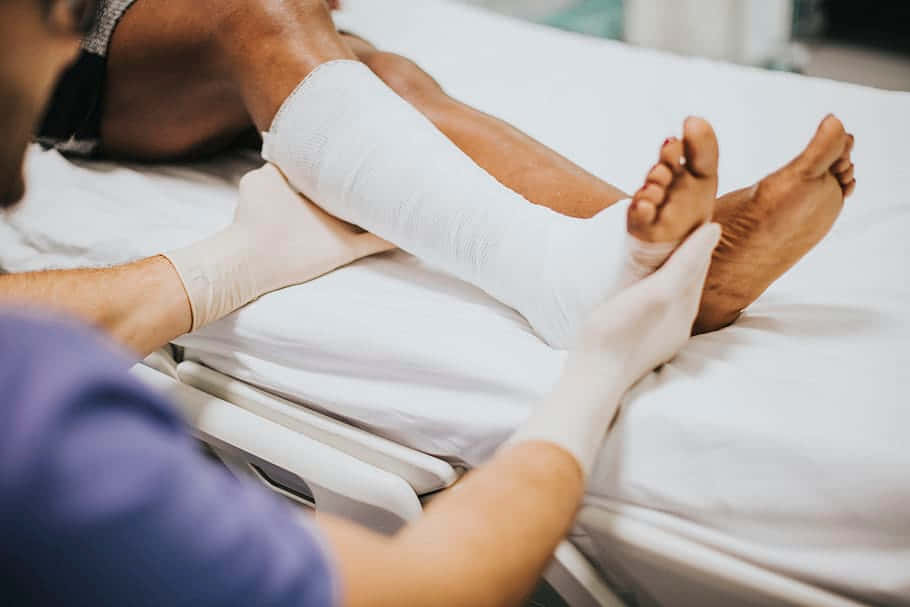 A Man Is Getting His Foot Bandaged In A Hospital Bed Background