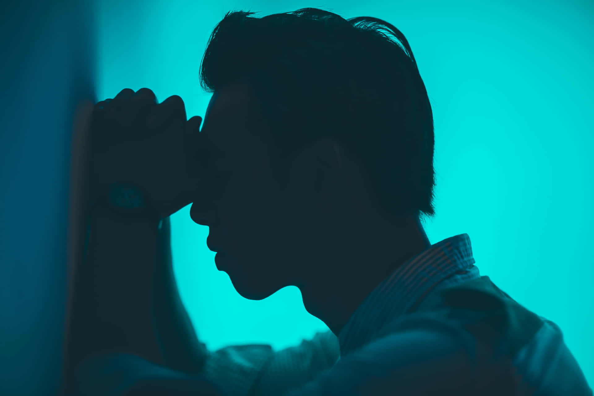 A Man Is Leaning Against A Wall With His Hand On His Face Background