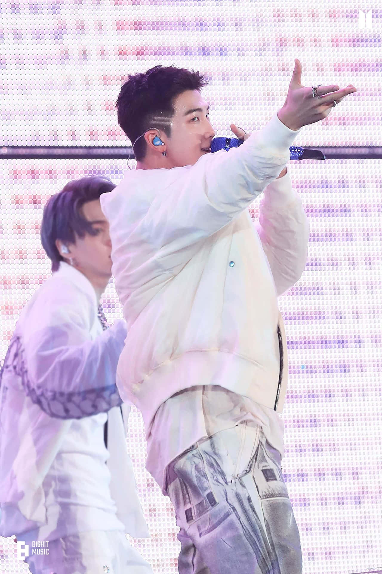 A Man Is Singing Into A Microphone While Another Man Is Standing Background
