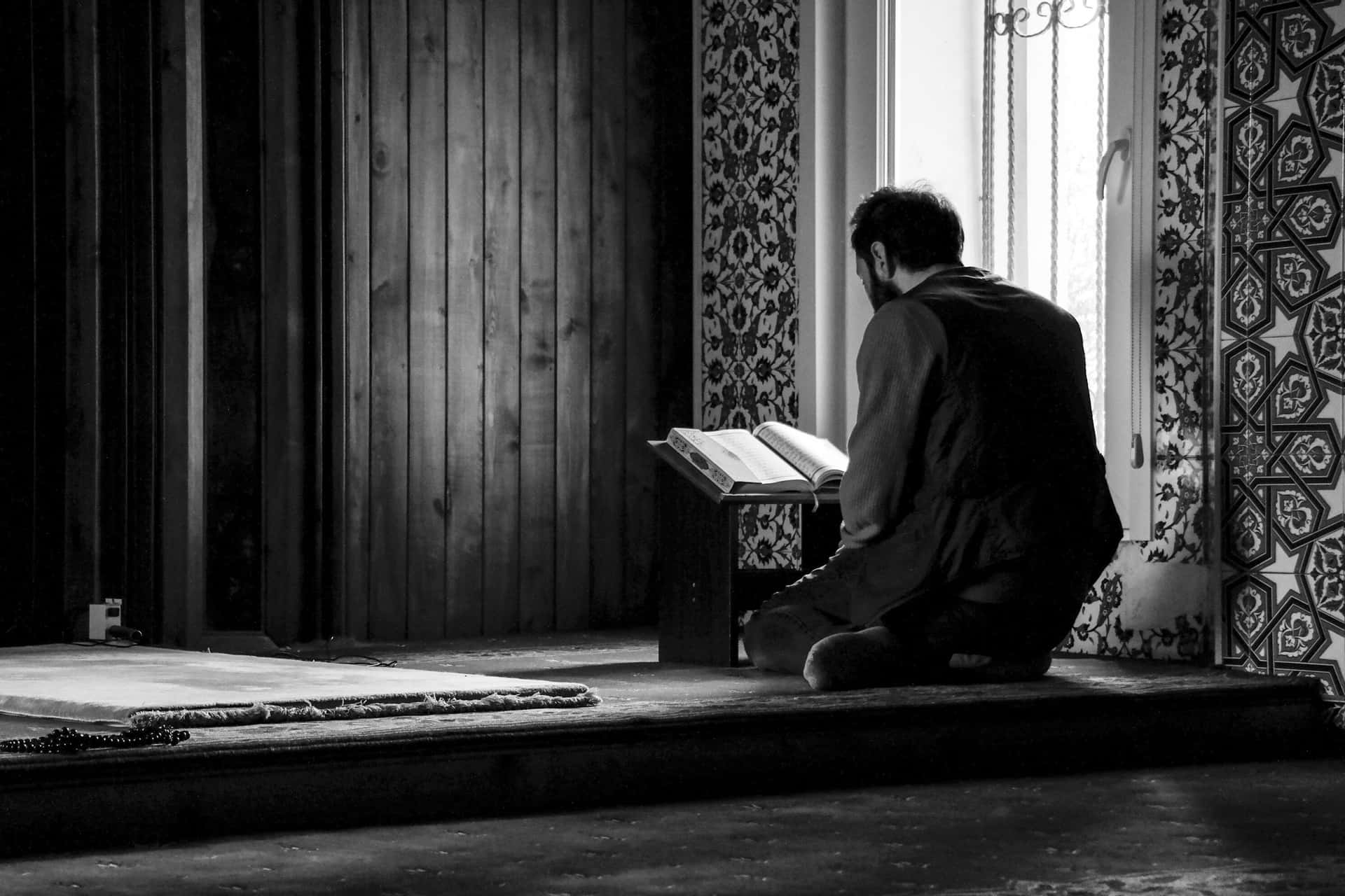 A Man Is Sitting In Front Of A Window Reading A Book Background