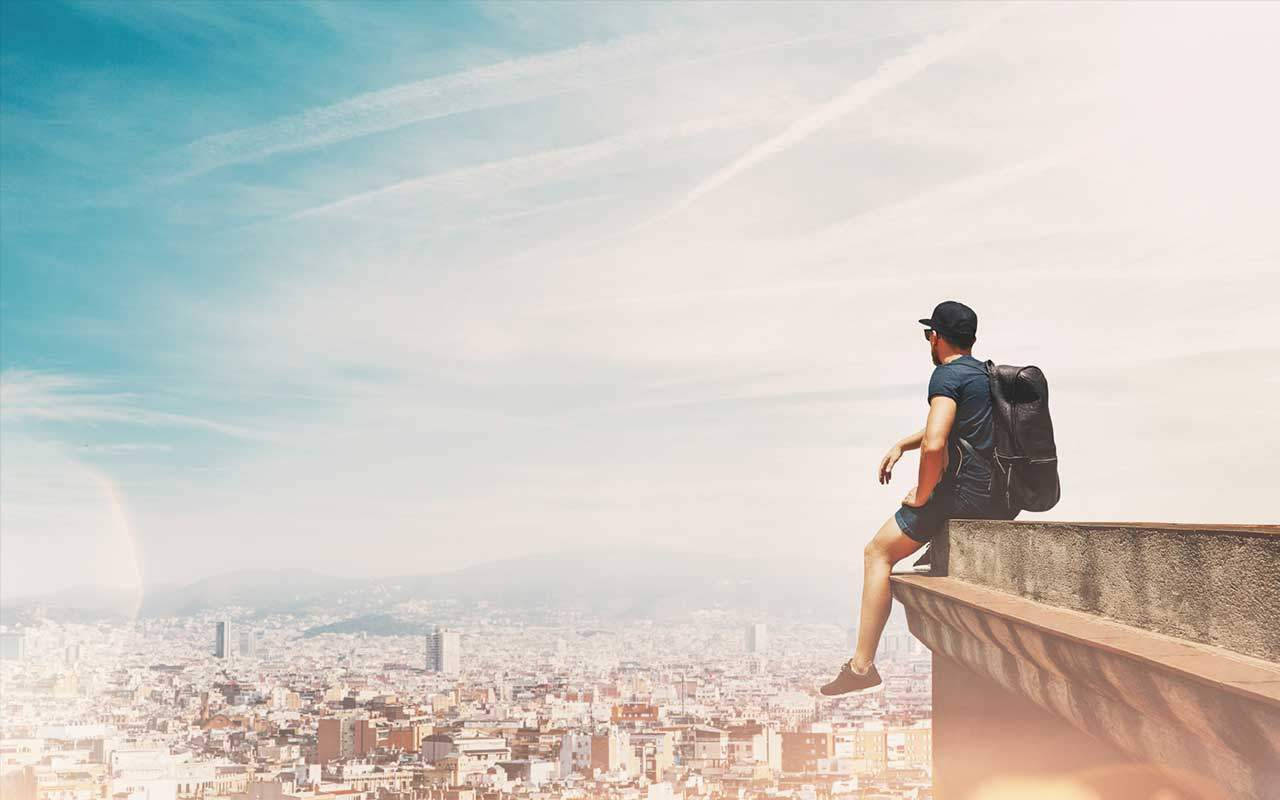 A Man Is Sitting On A Ledge Overlooking A City Background
