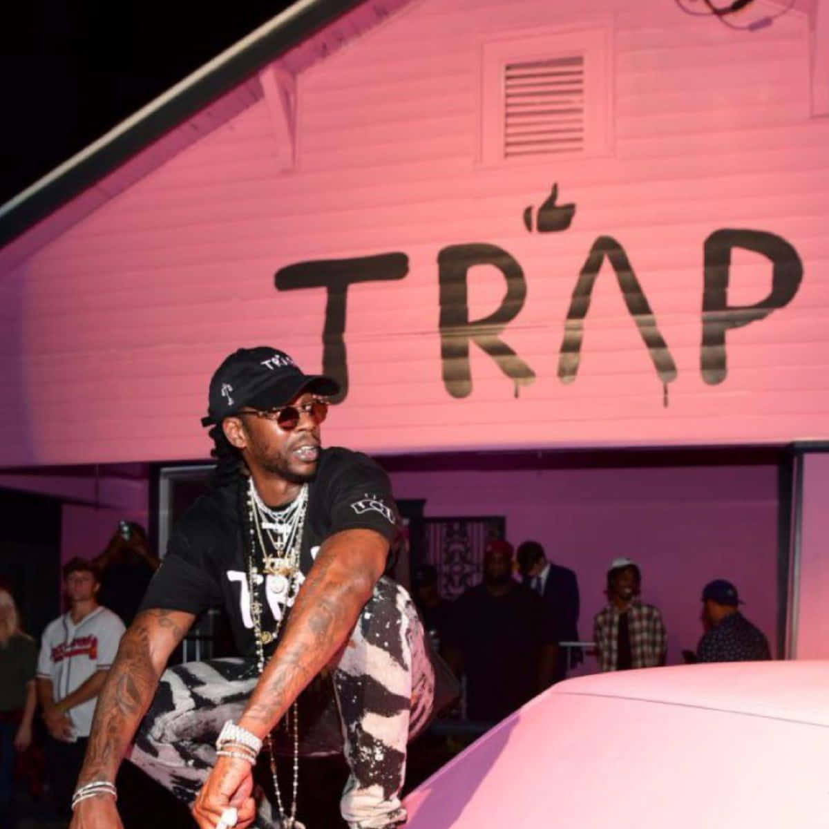 A Man Is Sitting On A Pink Car With A Sign That Says Trap Background