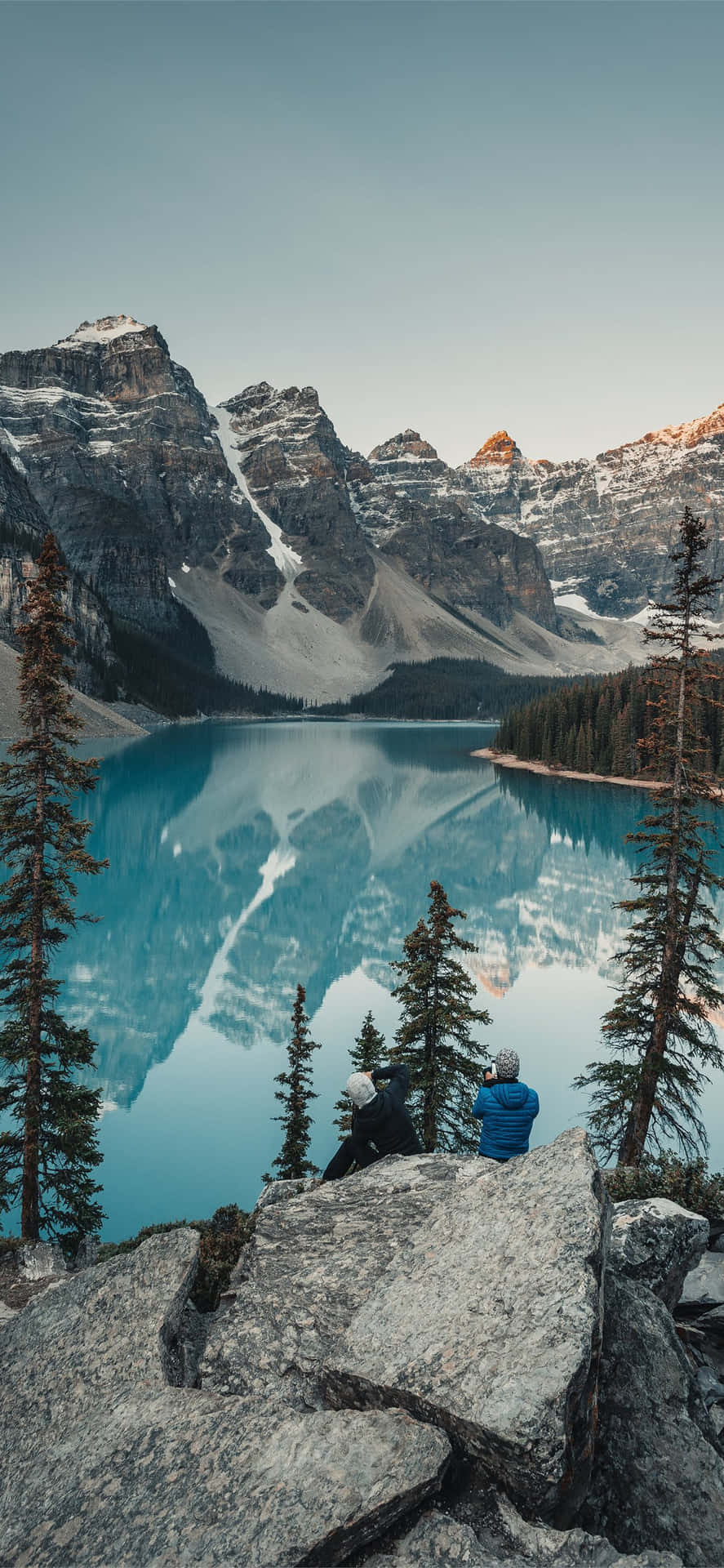 A Man Is Sitting On A Rock Overlooking A Lake Background