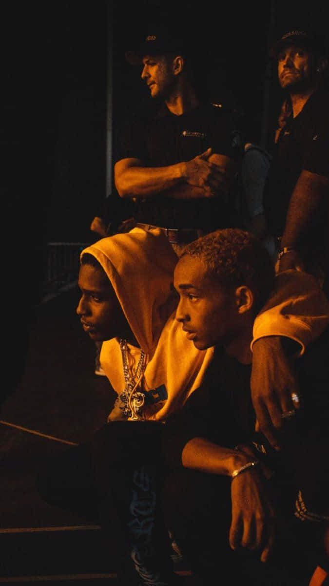 A Man Is Sitting On The Ground With A Man Behind Him