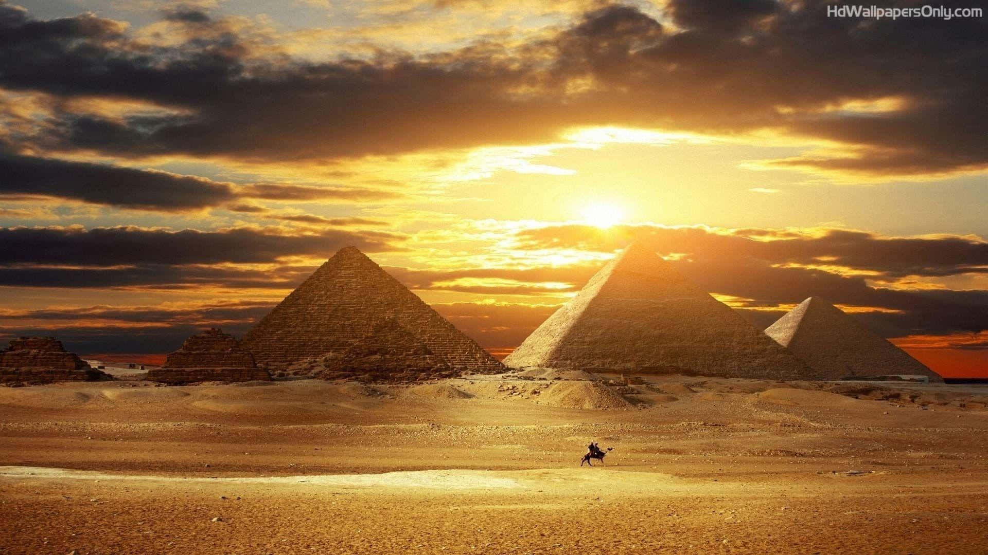 A Man Is Standing In Front Of The Pyramids At Sunset Background