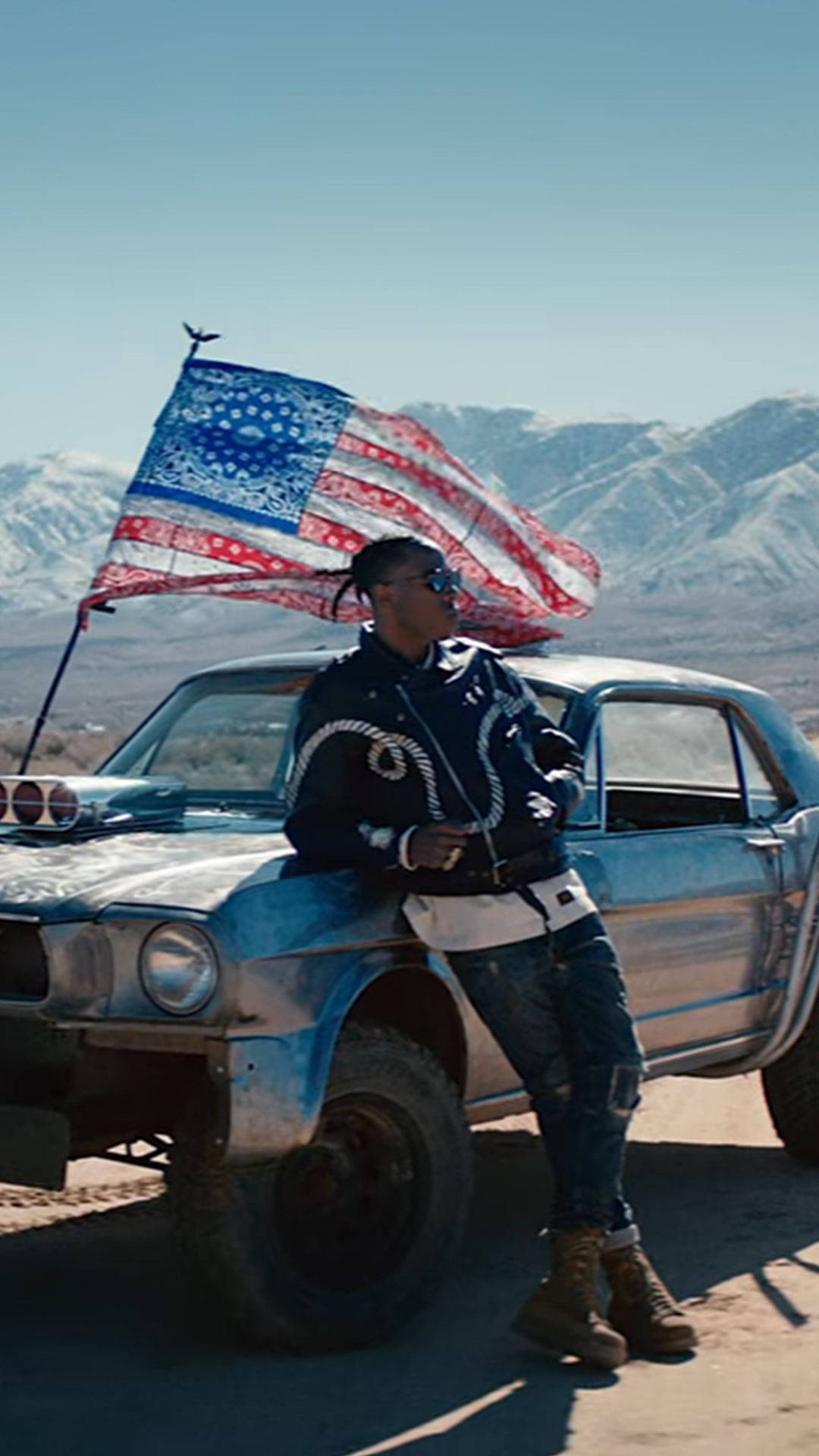 A Man Is Standing Next To A Blue Car With An American Flag Background