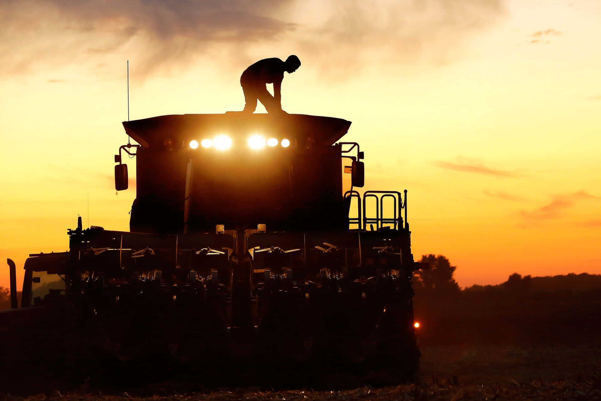A Man Is Standing On A Combine Harvester Background