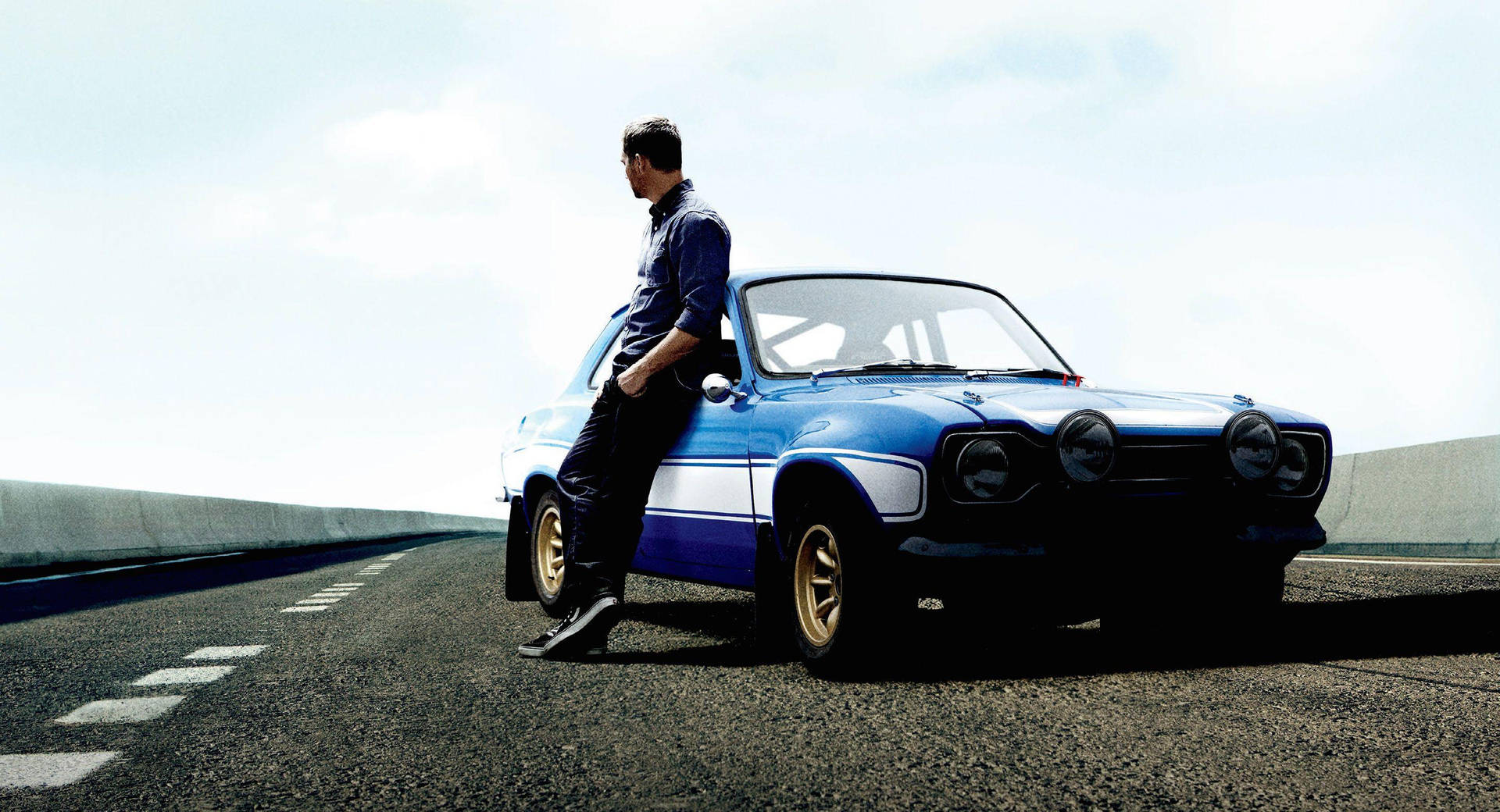 A Man Is Standing On The Side Of A Road With A Blue Car Background