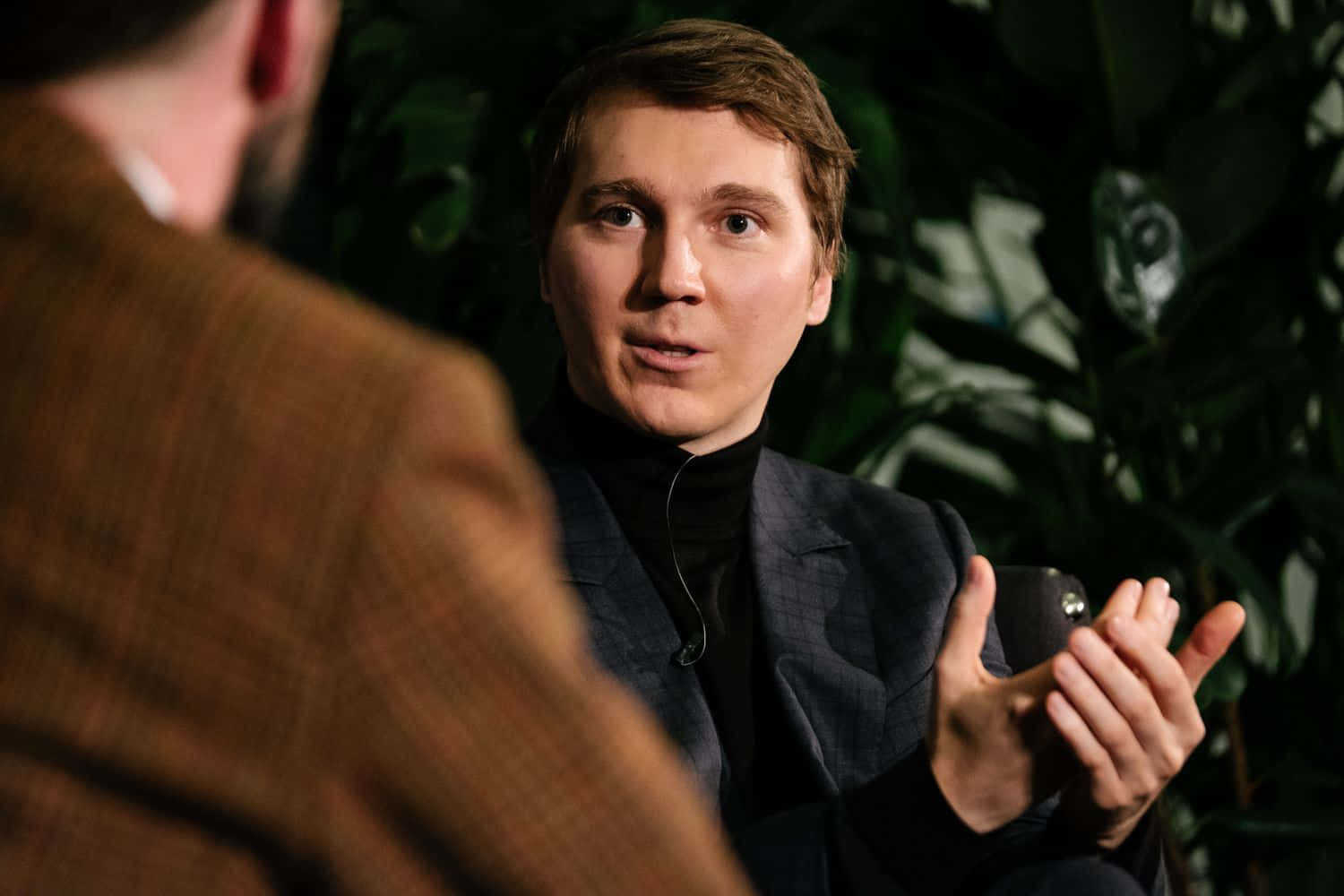A Man Is Talking To Another Man In A Suit Background