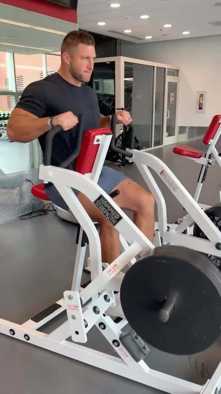 A Man Is Using A Rowing Machine In A Gym Background