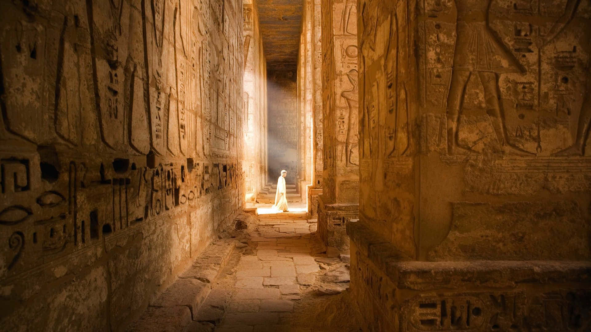 A Man Is Walking Down A Narrow Hallway In An Ancient Egyptian Temple Background