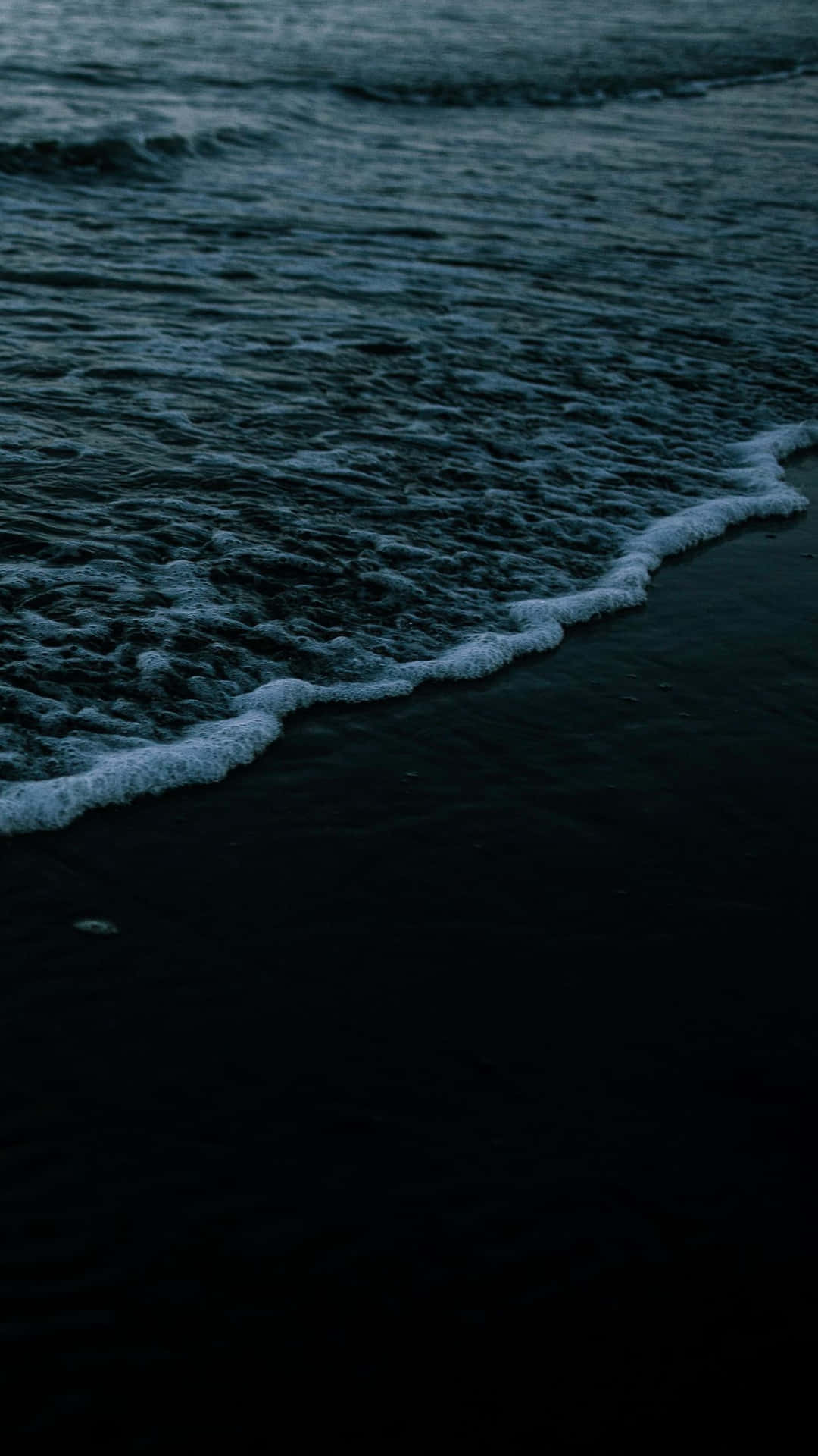 A Man Is Walking On The Beach At Dusk