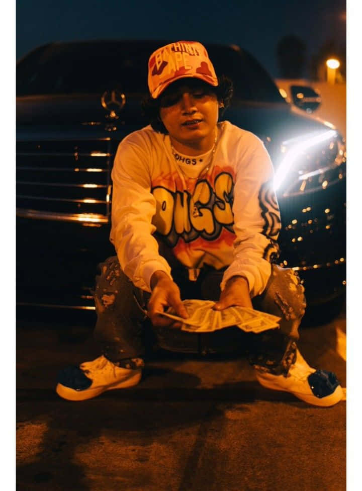 A Man Kneeling In Front Of A Car Holding Money Background