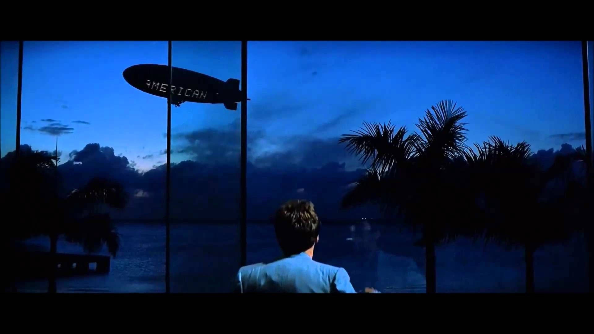 A Man Looking Out A Window At A Blimp Flying Over The Ocean Background