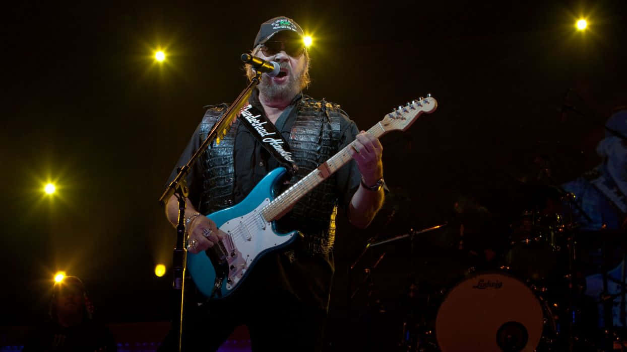 A Man Playing A Guitar On Stage Background