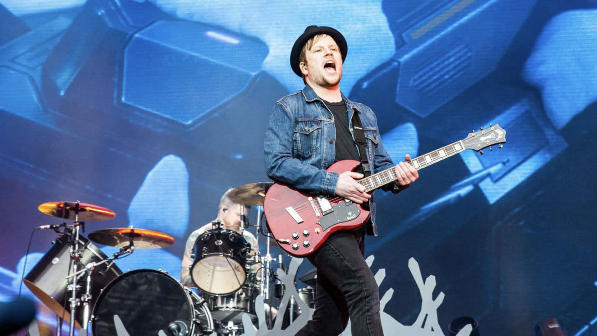 A Man Playing Guitar On Stage With A Microphone Background