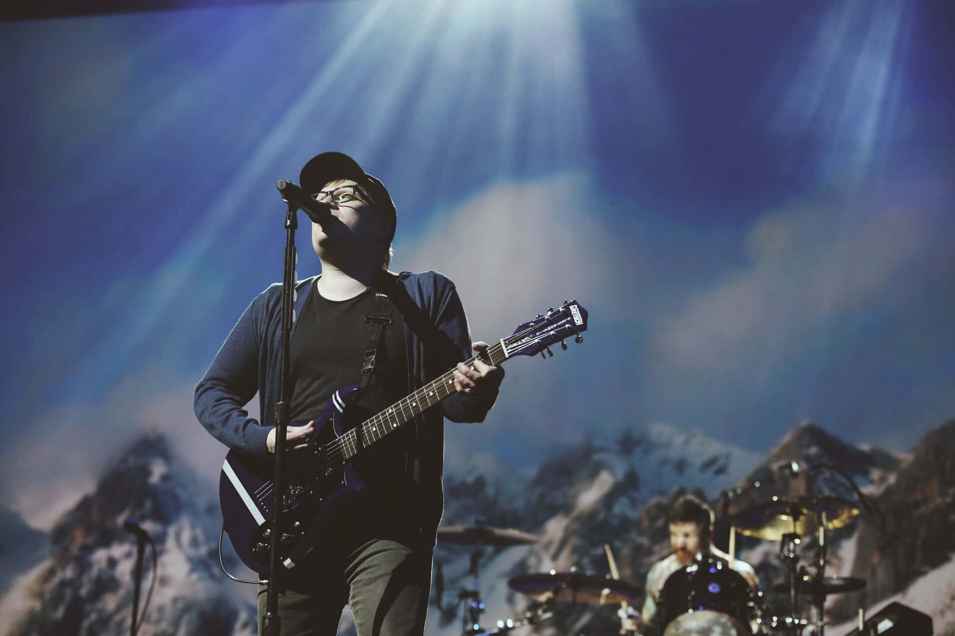 A Man Playing Guitar On Stage With A Microphone